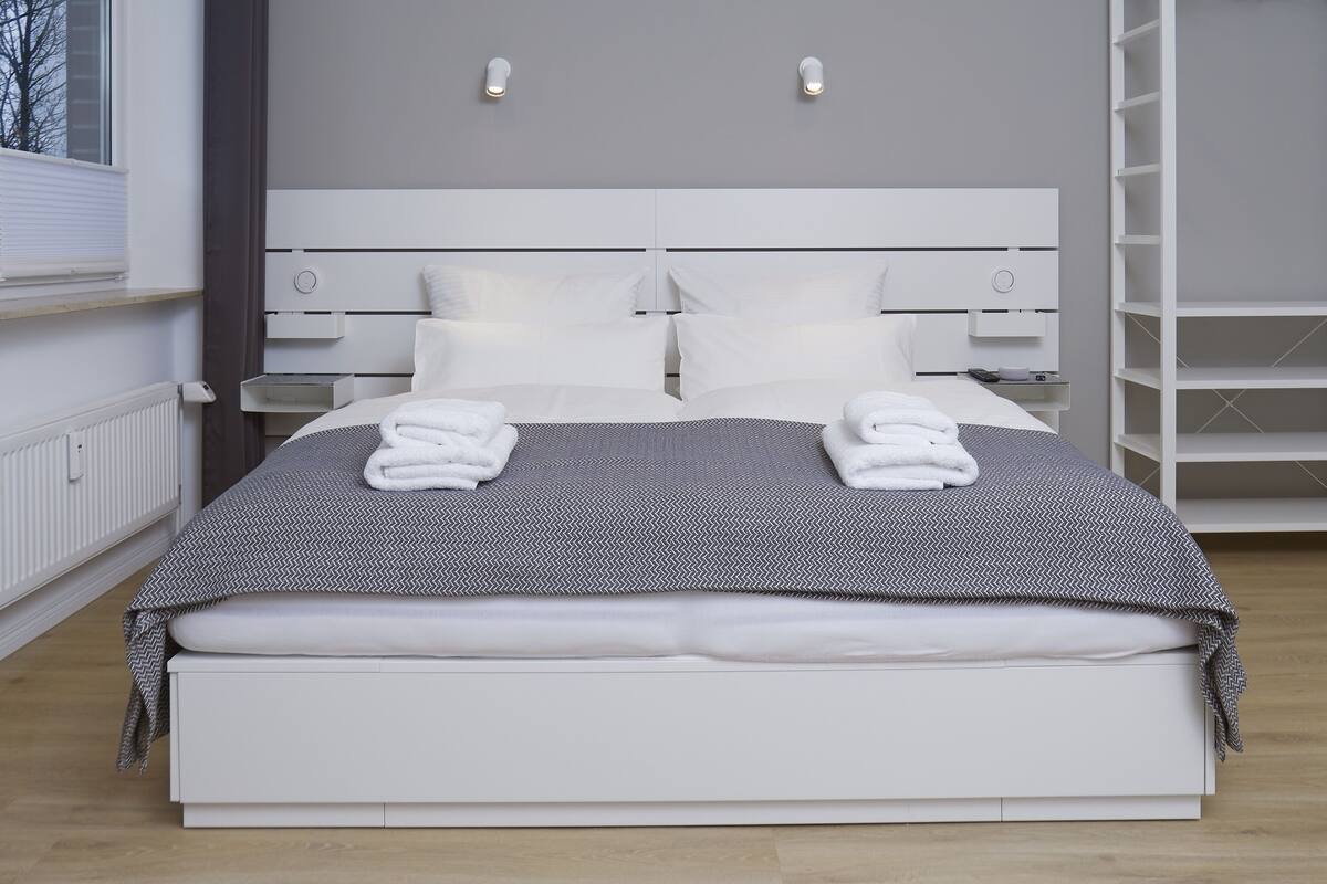Ein modernes Hotelzimmer mit einem großen Bett, einem weißen Kopfteil und Nachttischen.