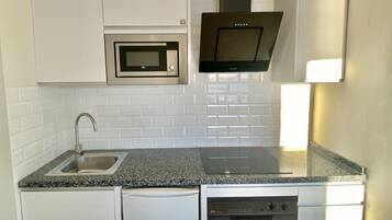 Una cucina compatta con mobili bianchi, forno a microonde integrato, piano cottura e lavastoviglie.