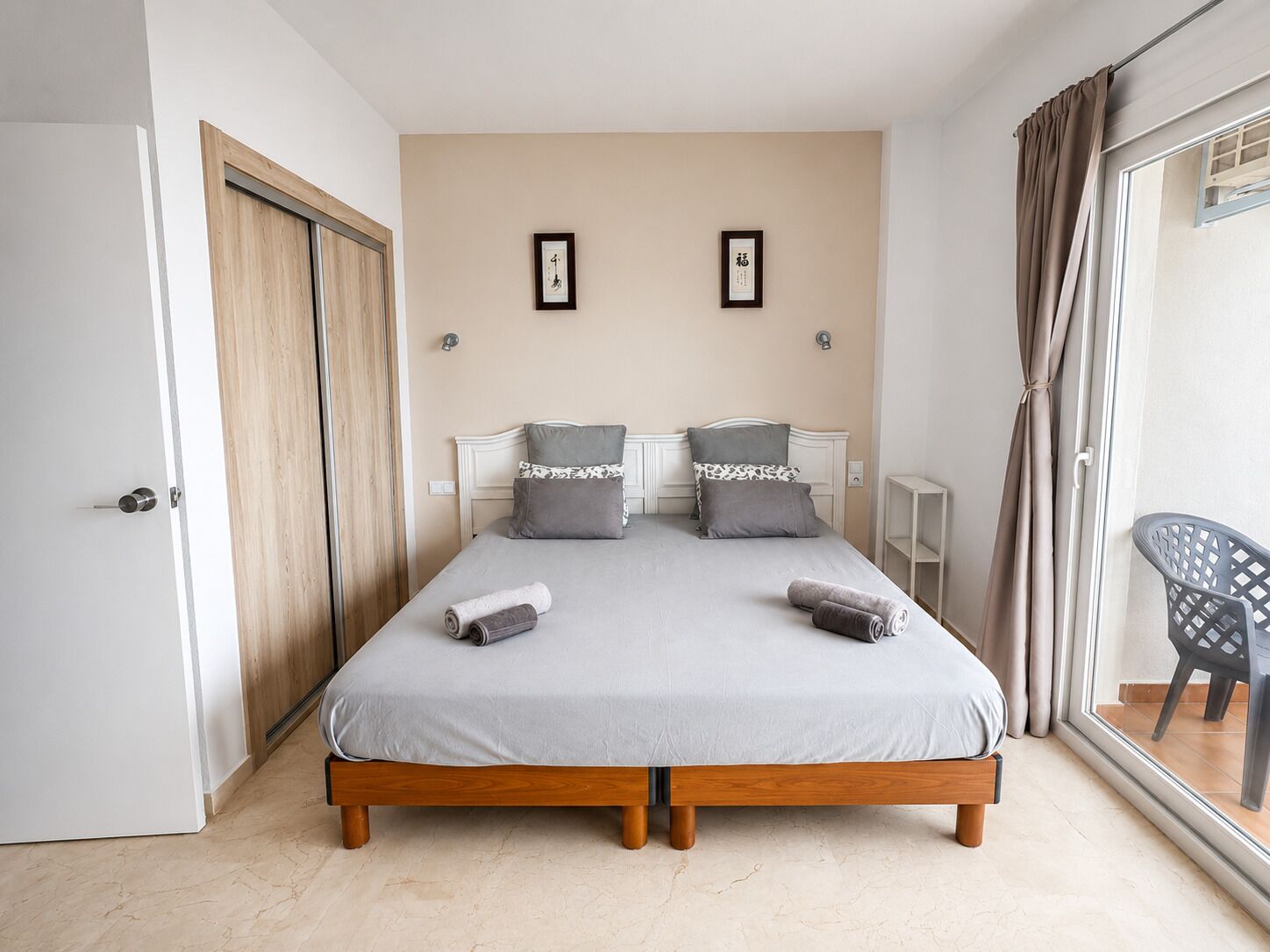 A bedroom with a bed, two pillows, a bedside table, a chair, and a door.