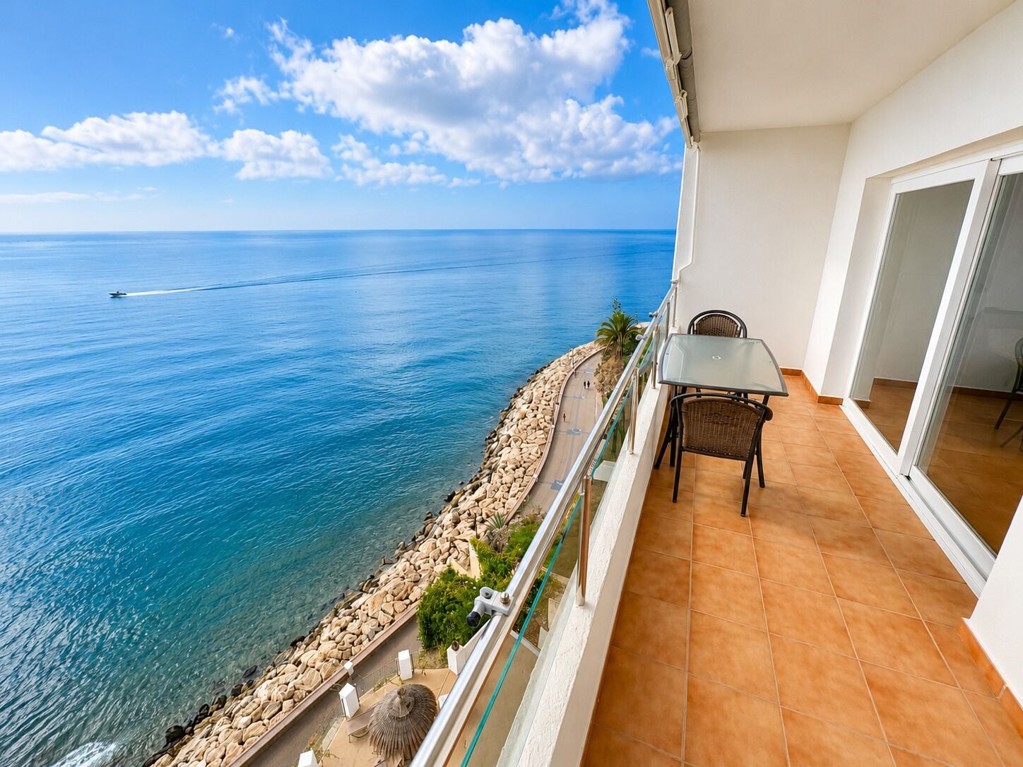 A balcony with a view of the sea, a table, and chairs.