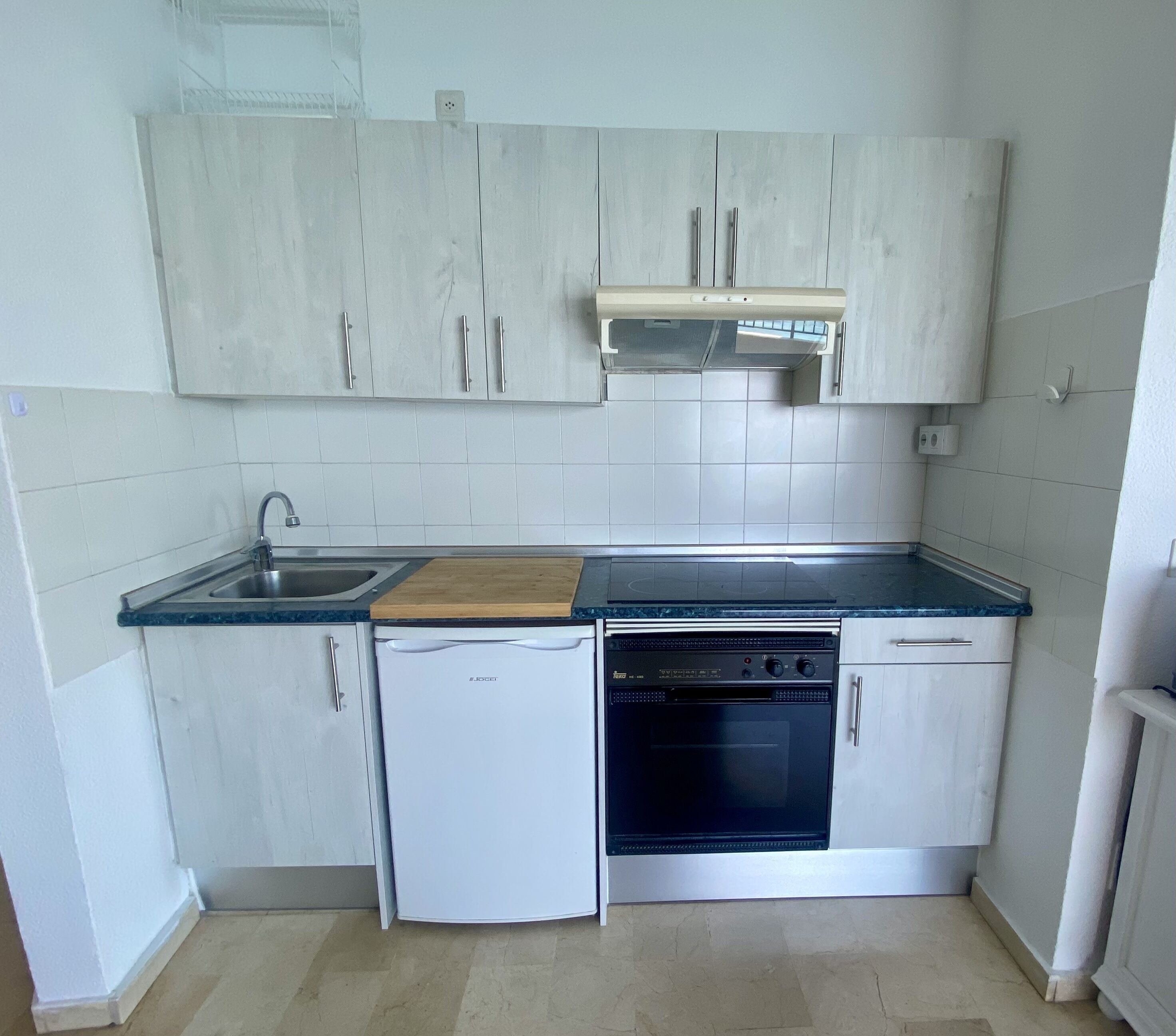 A compact kitchen with white cabinets, a built-in oven, a dishwasher, and a sink.