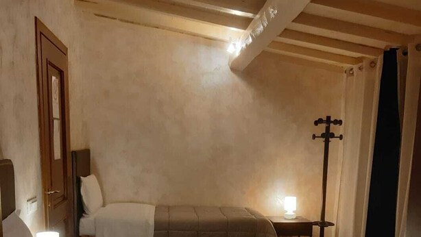 Une petite chambre à coucher, chaleureuse et accueillante, avec un lit simple, une table de chevet, une lampe et une armoire.