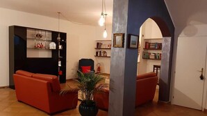 Un salon avec des canapés rouges, un meuble noir aux portes vitrées, une plante en pot et une bibliothèque.