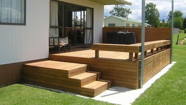 A modern house with a wooden deck, a covered patio, and a large sliding glass door leading to an outdoor seating area.