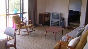 A hotel room with a large sliding glass door, a television, a small table, a sofa, and a rocking chair.