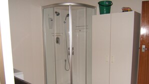 A corner shower enclosure with a glass door, a white wardrobe, and a green bucket on top of the wardrobe.