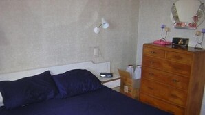 A bedroom with a bed, dresser, nightstand, lamp, and a mirror on the wall.