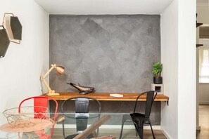 A modern workspace with a concrete wall, a desk, chairs, a lamp, and a potted plant.