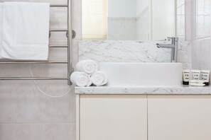 A bathroom with a marble sink, a towel rack with towels, and toiletries on the counter.
