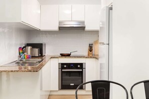 A modern kitchen with white cabinets, a stainless steel range hood, a microwave, a toaster, and an oven.