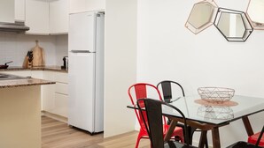 Une cuisine moderne avec des meubles blancs, un réfrigérateur blanc, une table à manger avec des chaises et des miroirs hexagonaux sur le mur.