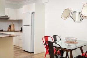A modern kitchen with white cabinets, a white refrigerator, a dining table with chairs, and hexagonal mirrors on the wall.