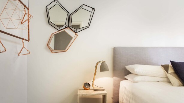 Une chambre à coucher comprenant un lit, une table de chevet, une lampe et trois miroirs fixés au mur.