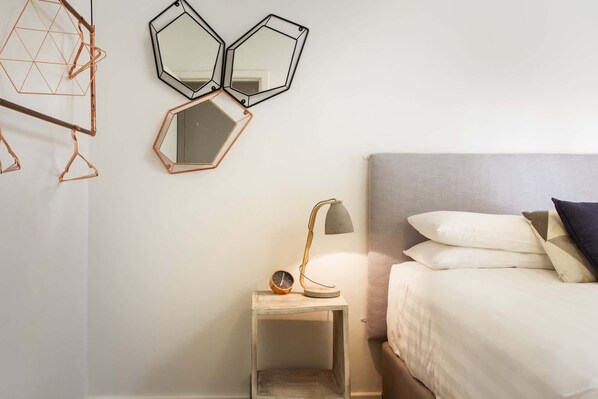 A bedroom with a bed, bedside table, lamp, and three wall-mounted mirrors.