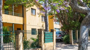 Un immeuble avec un balcon, un arbre aux fleurs violettes et une voiture garée.