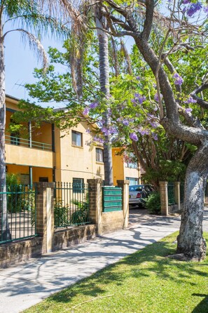 A building with a balcony, a tree with purple flowers, and a parked car.