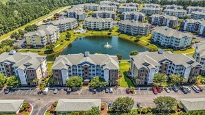 An aerial view of a residential complex with multiple apartment buildings, a central pond, and a parking area. - Myrtlewood Villa Lake View 2BR/2fullBA in Central Myrtle Beach (Myrtle Beach)