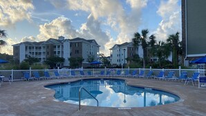 A pool area with lounge chairs and umbrellas, surrounded by a white fence and buildings in the background. - Myrtlewood Villa Lake View 2BR/2fullBA in Central Myrtle Beach (Myrtle Beach)