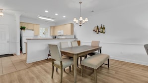 A dining area with a wooden table and chairs, a chandelier, and a kitchen in the background. - Myrtlewood Villa Lake View 2BR/2fullBA in Central Myrtle Beach (Myrtle Beach)