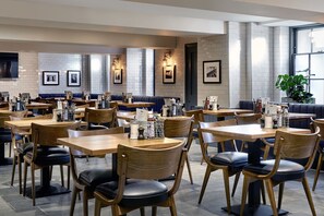 A restaurant with multiple tables and booths, wooden chairs, and a tiled wall with framed pictures. - The George (Cheltenham)