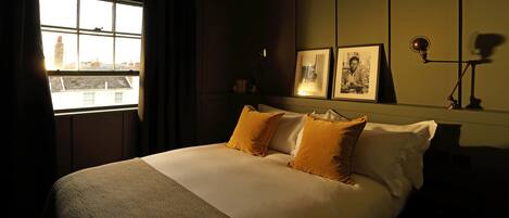 A neatly made bed with a patterned bedspread and two pillows, a bedside lamp, and framed pictures on the wall.