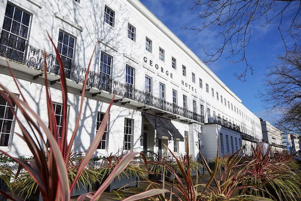 A white building with the name "GEORGE HOTEL" on the facade, featuring multiple windows and balconies with black railings. - The George (Cheltenham)