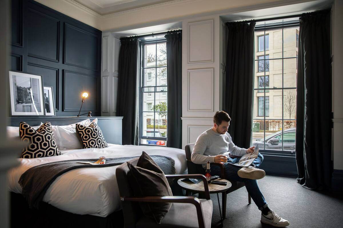 A modern hotel room with a large bed, a small table, and a window with curtains.