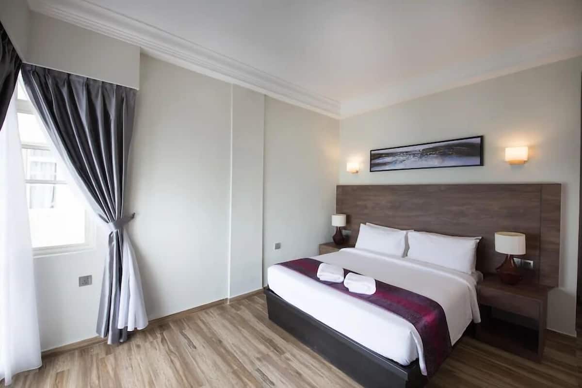 A hotel room with a large bed, a headboard with a mounted artwork, bedside lamps, and a window with curtains.