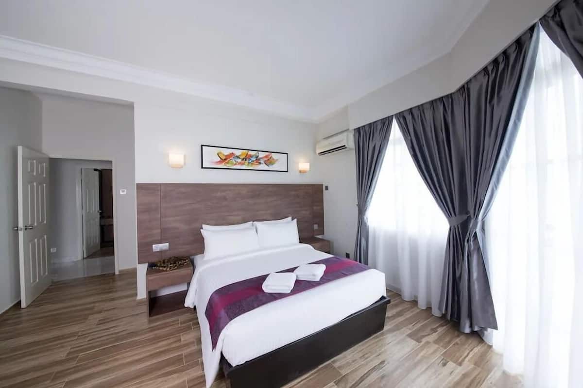 A hotel room with a bed, a bench, a wall-mounted artwork, and a large window with curtains.