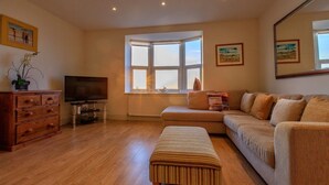 Ein Wohnzimmer mit einer Couch, einem Fernseher, einer Holzkabine und einem Fenster mit Blick.
