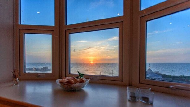 Ein Zimmer mit Blick auf den Sonnenuntergang über dem Meer, eine Obstschale am Fensterbrett und zwei Gläser.