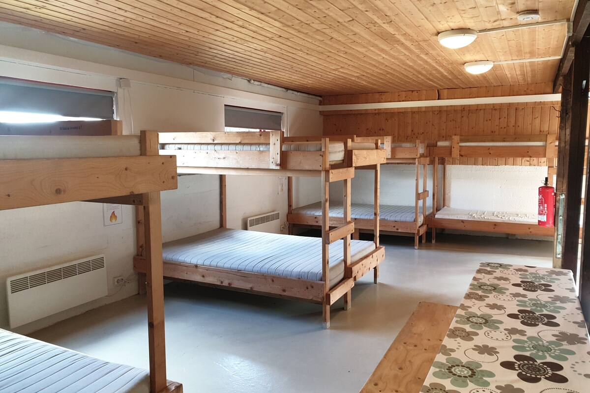 A bunk bed room with wooden ceilings and walls, a radiator, and a fire extinguisher.