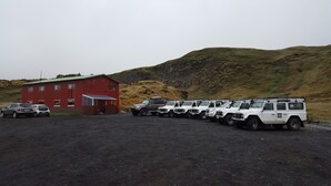 A row of white off-road vehicles parked in front of a red building with a green roof. - Hólaskjól Highlandcenter (Kirkjubaejarklaustur)