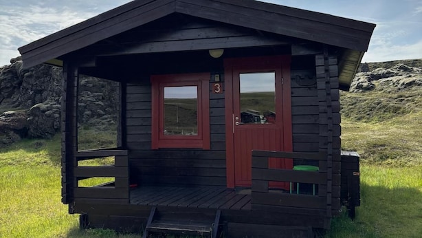 A small wooden cabin with a porch, a door, and a window. - Hólaskjól Highlandcenter (Kirkjubaejarklaustur)