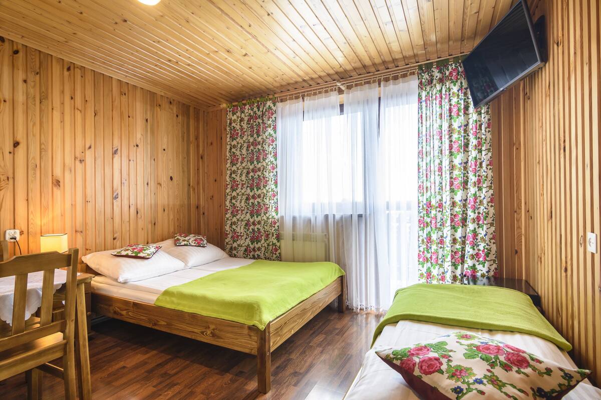 A wooden-paneled room with a bed, a chair, and a television mounted on the wall.
