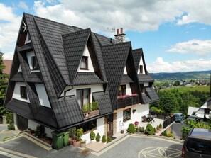 A traditional chalet with a steeply pitched roof, a stone chimney, and a balcony with potted plants. - Pokoje gościnne Wilczek (Bukowina Tatrzanska)