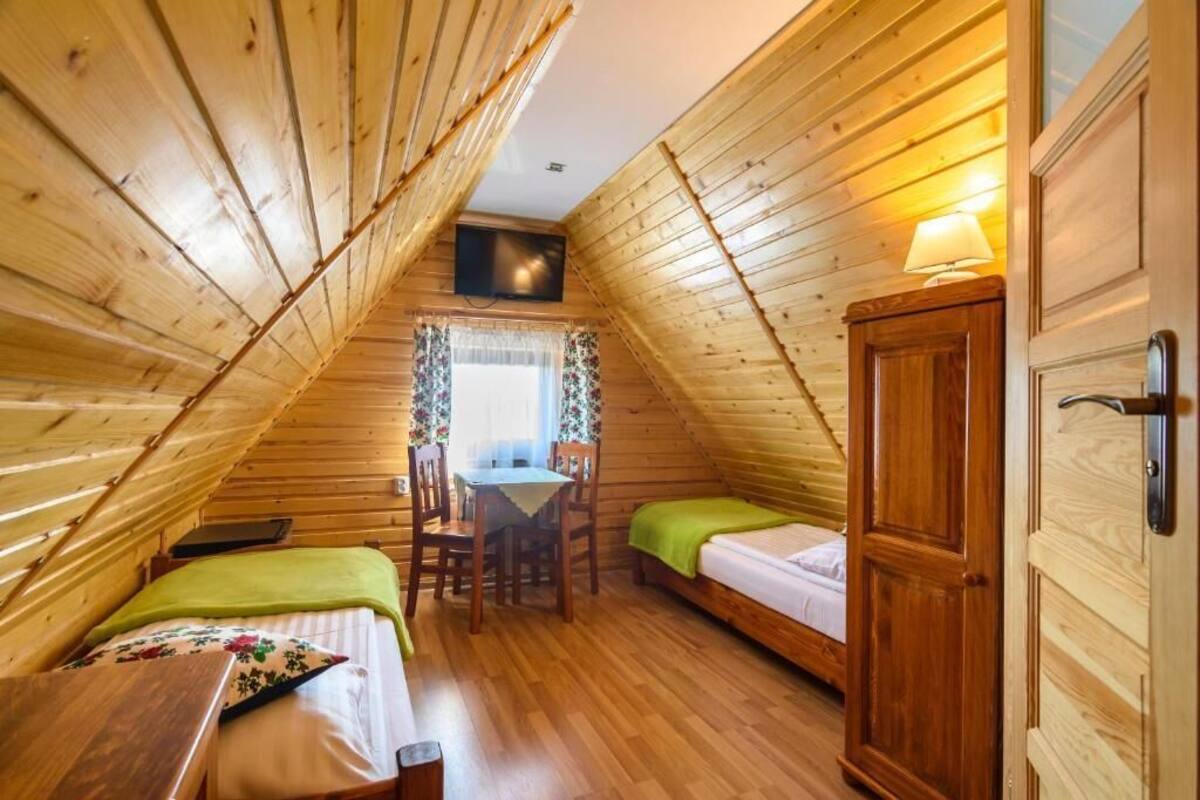 A cozy attic bedroom with wooden walls, a bed, a desk, and a chair.