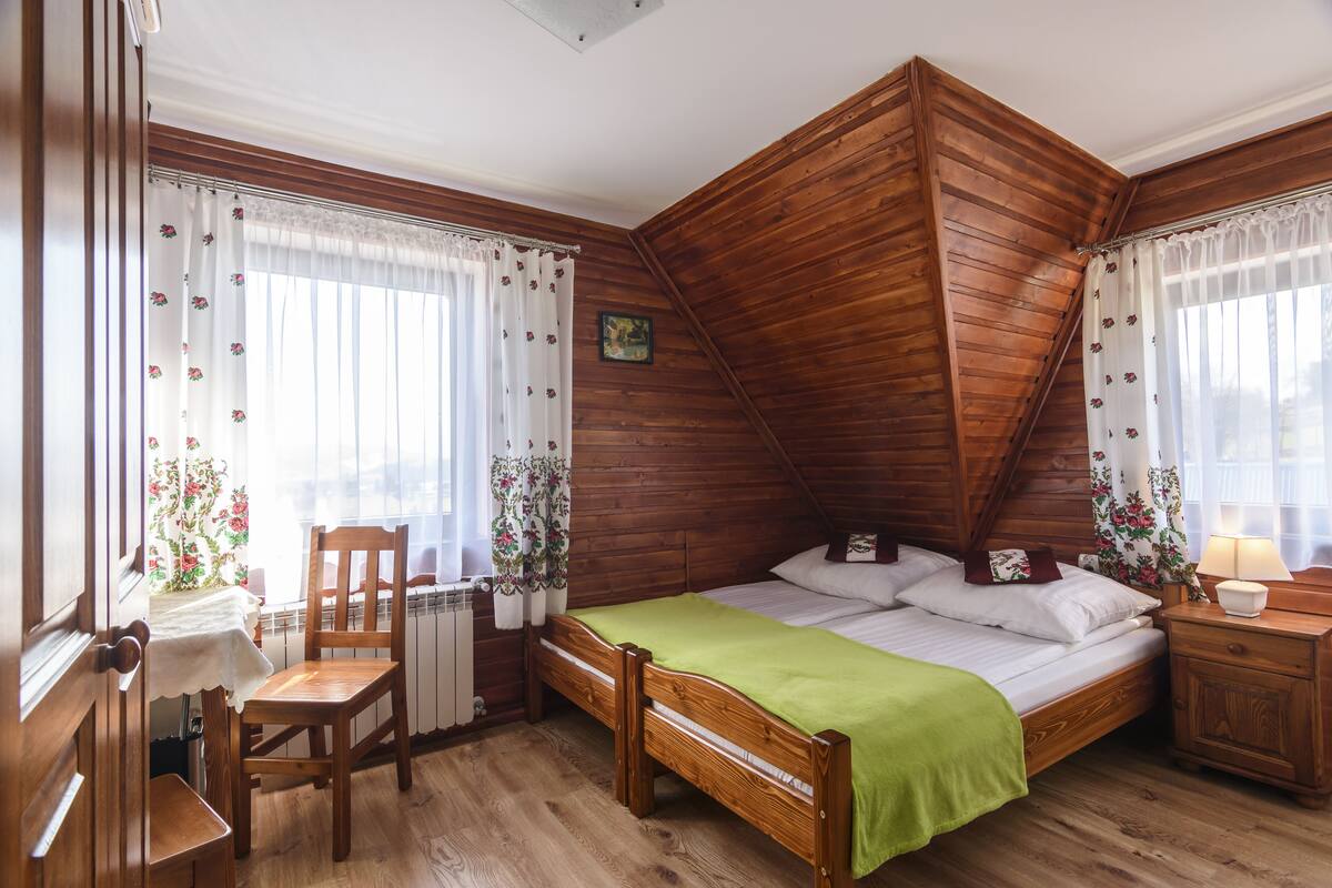 A wooden room with a bed, a chair, a table, and a radiator.