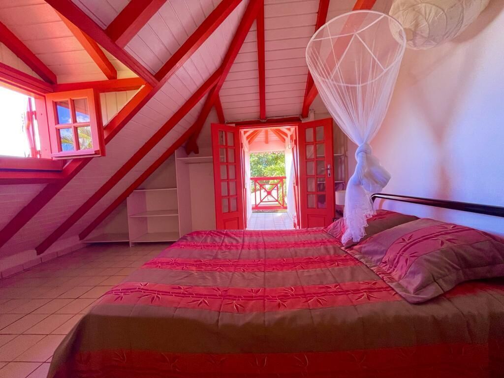 Un dormitorio con una cama grande, una ventana con marco rojo y vistas al exterior.