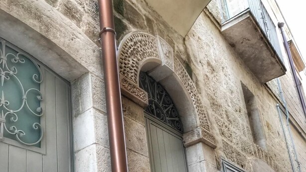 Un edificio de piedra con una tubería de metal, un ventanal decorativo y una puerta.