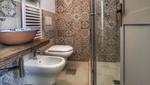 Un baño con inodoro blanco, bidé y zona de ducha con mampara de vidrio.