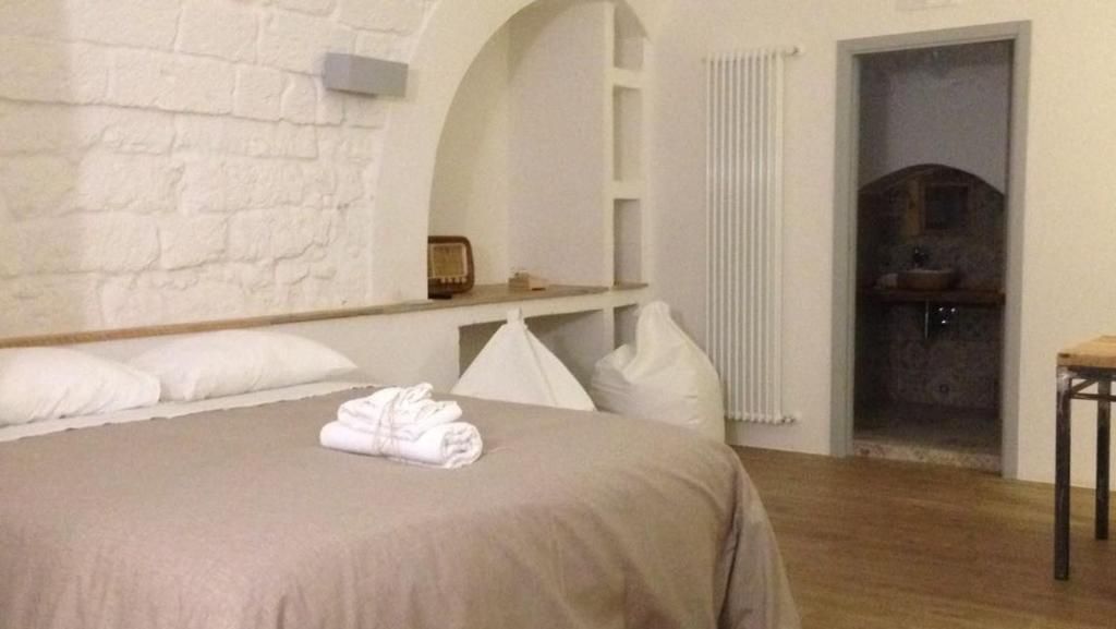 Une chambre à coucher avec un lit, des oreillers blancs, une serviette pliée, une table de chevet en bois, une radio, un radiateur blanc et une porte de salle de bain.