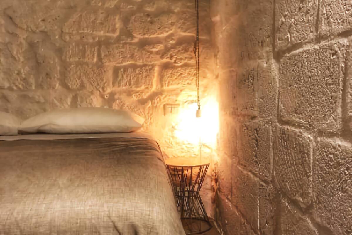 Una habitación pequeña con paredes de piedra, una cama y una mesita.