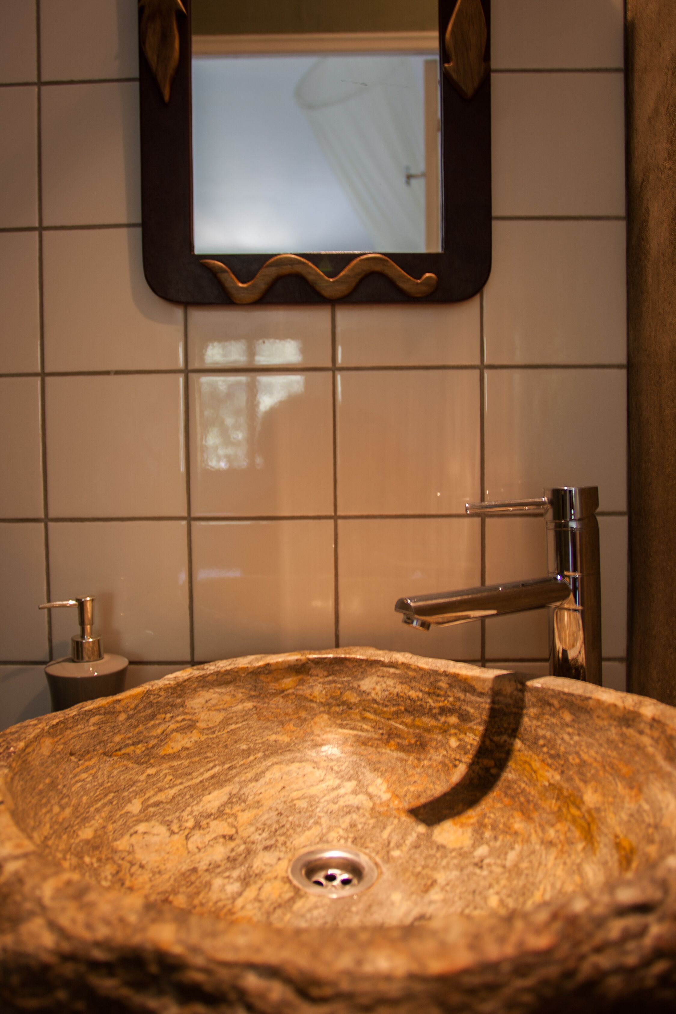 Ein Badezimmer mit einem großen, ovalen Waschbecken aus Stein, einem Spiegel darüber und einem kleinen Beistelltisch mit einer Seifenspender.