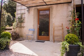 A covered patio with a wooden door, a blue folding chair, and potted plants. - Les deux chemins (Mons)