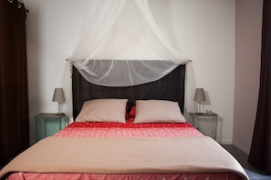A neatly made bed with a canopy, two bedside tables with lamps, and a red and white patterned bedspread. - Les deux chemins (Mons)