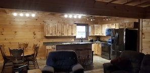 A wooden cabin interior with a kitchen featuring wooden cabinets, a dining table with chairs, a bar area with stools, and a large refrigerator. - Beautiful 3 bed / 3 bath Luxury Cabin, Hot Tub, Games, Easy Check in! Book Now! (Sevierville)