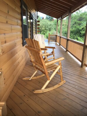 A wooden rocking chair on a covered porch with a wooden deck and a view of greenery. - Beautiful 3 bed / 3 bath Luxury Cabin, Hot Tub, Games, Easy Check in! Book Now! (Sevierville)