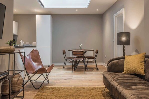 A modern living room with a sofa, a dining table with chairs, a kitchen area, and a skylight. - Nelson West- Modern one bed, great for long stays (Ramsgate)
