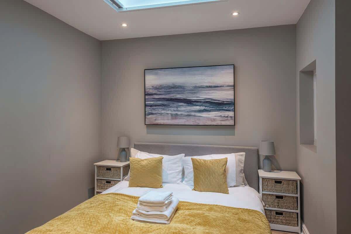 A modern bedroom with a large bed, a wall-mounted painting, and bedside tables with lamps.